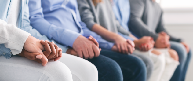A close-up shot shows a row of people sitting together, holding hands. The subjects are partially visible from the waist up, wearing casual clothing in blue, gray, and white. This image evokes feelings of connection, support, and unity.