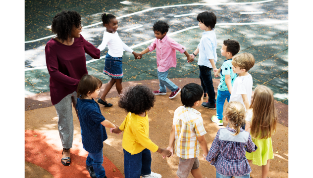 Group of children in playground with teacher walking in a circle holding hands