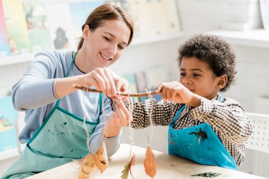 happy teacher and young child holding a stick with leaves hanging