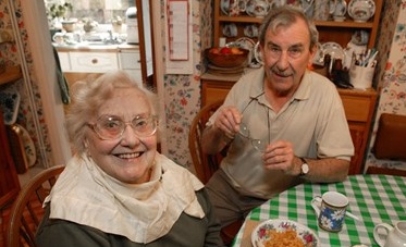Man and woman sitting at a table with a cup of tea, and bowl of food.