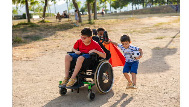 young boy in a wheelchair playing with two young boys, one is holding a football.