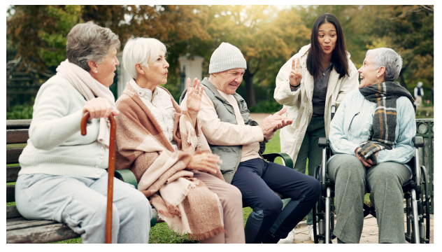 Group of people sitting on a park bench with one lady sitting in a wheelchair speaking with young person