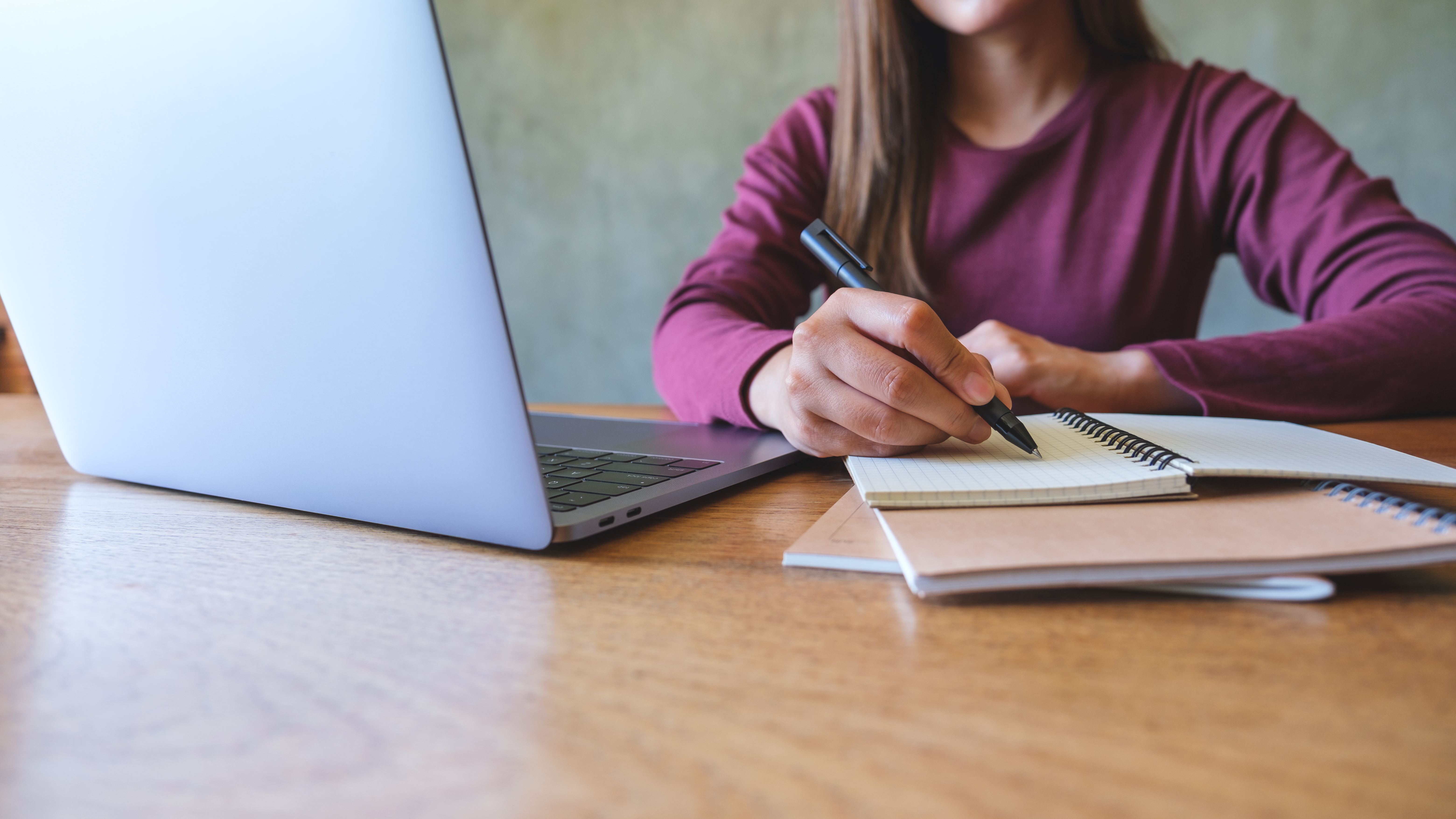 Young person sitting at a desk in front of computer, writing in a notebook